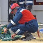 Maintenance - man in red and black jacket wearing black pants and red helmet holding green and black